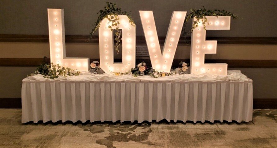 The letters L O V E lit on top of white skirted table with greenery