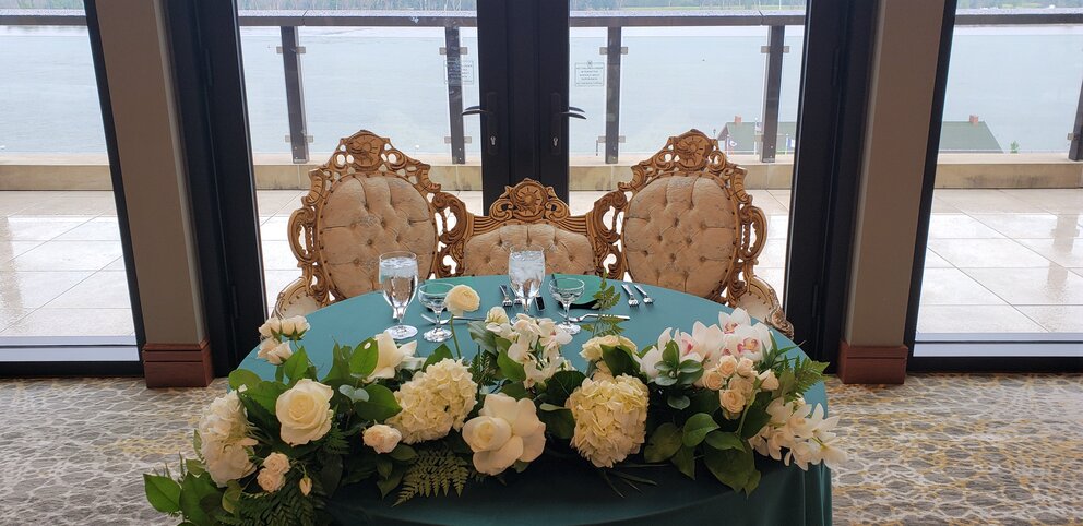 Wedding sweetheart table with two grand white chairs set behind a green table with white flowers