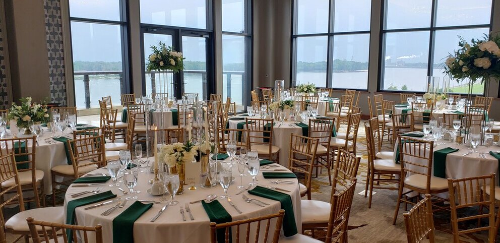 Banquet tables set with white linens, green napkins, and gold accents with white flower bouquets in the center