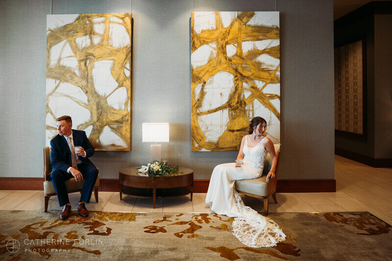 A bride and a groom sitting on chairs in the lobby of The Merrill Hotel