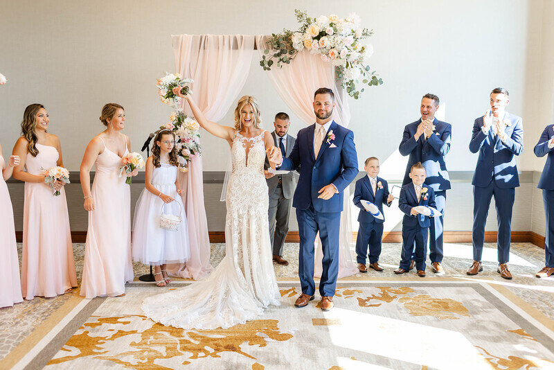 A bride and groom with their wedding party in front of a floral arch